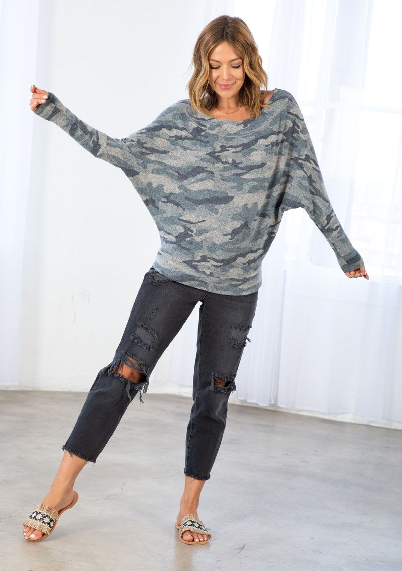 [Color: Olive/Sage] A model wearing an ultra soft Hacci knit pullover in a camouflage print. With long tapered dolman sleeves and a boat neckline that can be worn on or off the shoulder. 