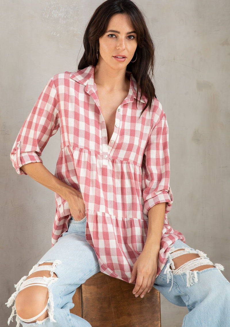 [Color: Dusty Rose/White] A model wearing a relaxed cotton blend pink large gingham button up tunic, with a rolled sleeve, a tiered body, and a long tunic length. 