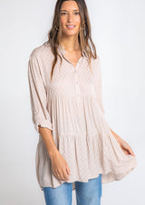 [Color: Tan] A model wearing a relaxed textured checkered jacquard button up tunic, with a rolled sleeve, a tiered body, and a long tunic length.