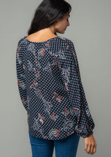 [Color: Charcoal/Dusty Blue] A back facing image of a brunette model wearing a charcoal grey and light blue floral paisley print bohemian blouse. With long sleeves and a v neckline. 