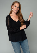 [Color: Black] A front facing image of a red headed model wearing a black bohemian peasant top in embroidered chiffon. With long sleeves, lattice trim, a v neckline, a button front, and a flowy relaxed fit. 
