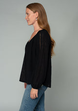 [Color: Black] A side facing image of a red headed model wearing a black bohemian peasant top in embroidered chiffon. With long sleeves, lattice trim, a v neckline, a button front, and a flowy relaxed fit. 