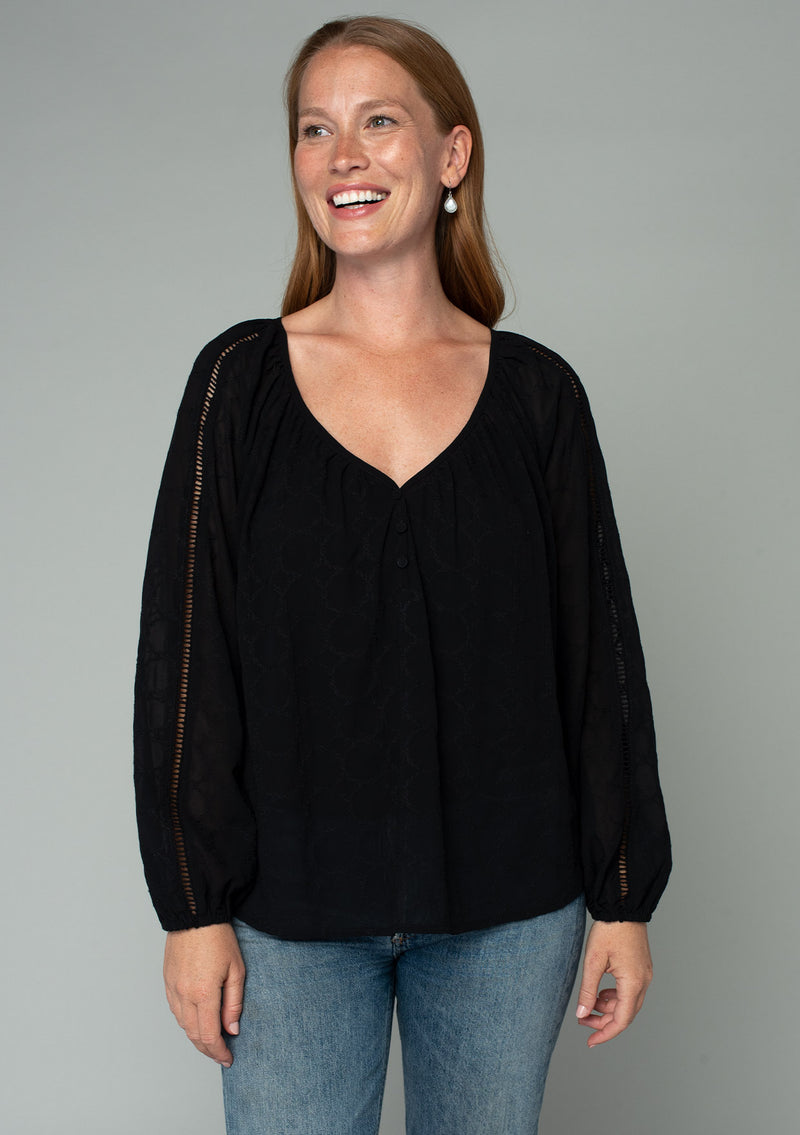 [Color: Black] A half body front facing image of a red headed model wearing a black bohemian peasant top in embroidered chiffon. With long sleeves, lattice trim, a v neckline, a button front, and a flowy relaxed fit. 