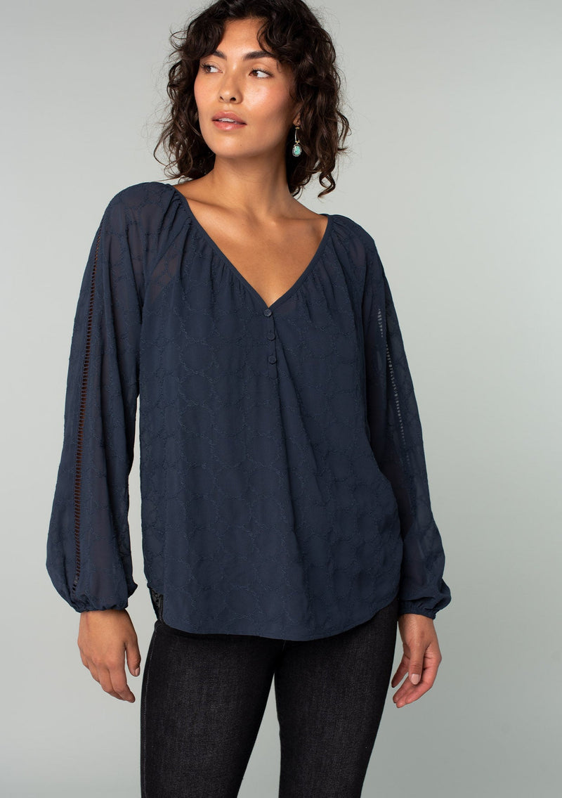 [Color: Ink Blue] A half body front facing image of a brunette model wearing a navy blue bohemian peasant top in embroidered chiffon. With long sleeves, lattice trim, a v neckline, a button front, and a flowy relaxed fit. 