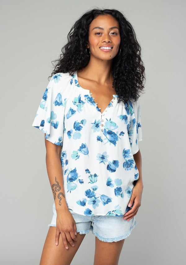 [Color: Ivory/Aqua] A front facing image of a brunette model wearing a classic bohemian spring to in an ivory white and blue floral print top. With short flutter sleeves and a loop button front. 