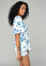 [Color: Ivory/Aqua] A side facing image of a brunette model wearing a classic bohemian spring to in an ivory white and blue floral print top. With short flutter sleeves and a loop button front. 