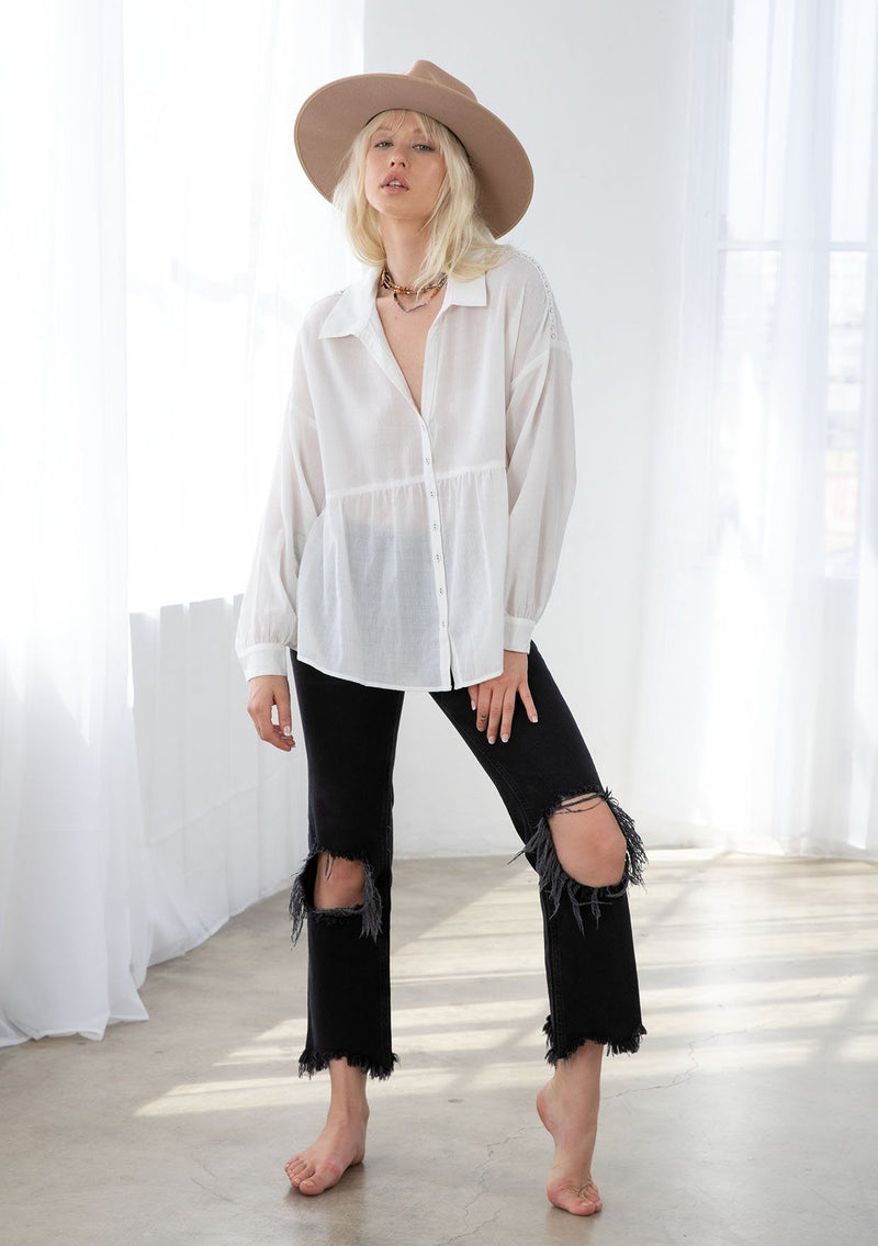 [Color: White] A model wearing a sheer bohemian white button up shirt. With voluminous long sleeves, a button cuff, a tiered body, and a lace trim detail along the shoulder. 