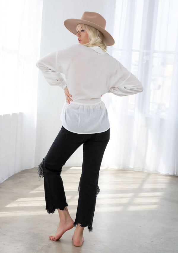 [Color: White] A model wearing a sheer bohemian white button up shirt. With voluminous long sleeves, a button cuff, a tiered body, and a lace trim detail along the shoulder. 