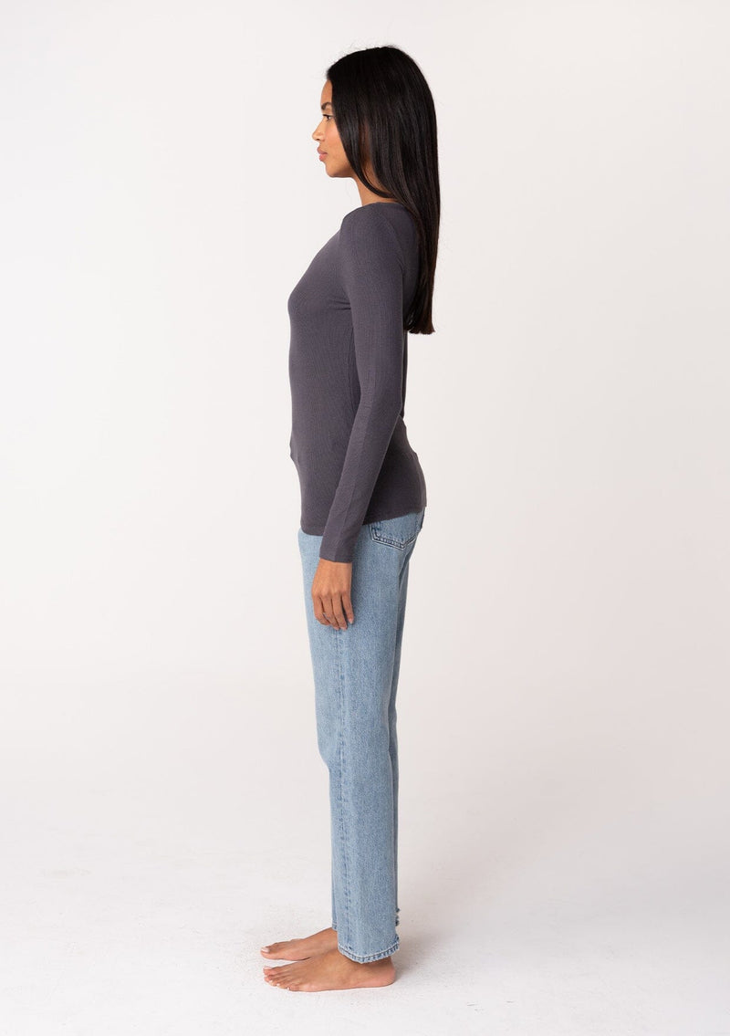 [Color: Charcoal] A side facing image of a brunette model wearing a charcoal grey bamboo micro ribbed long sleeve tee. Featuring a mock neckline and a stretchy slim fit.