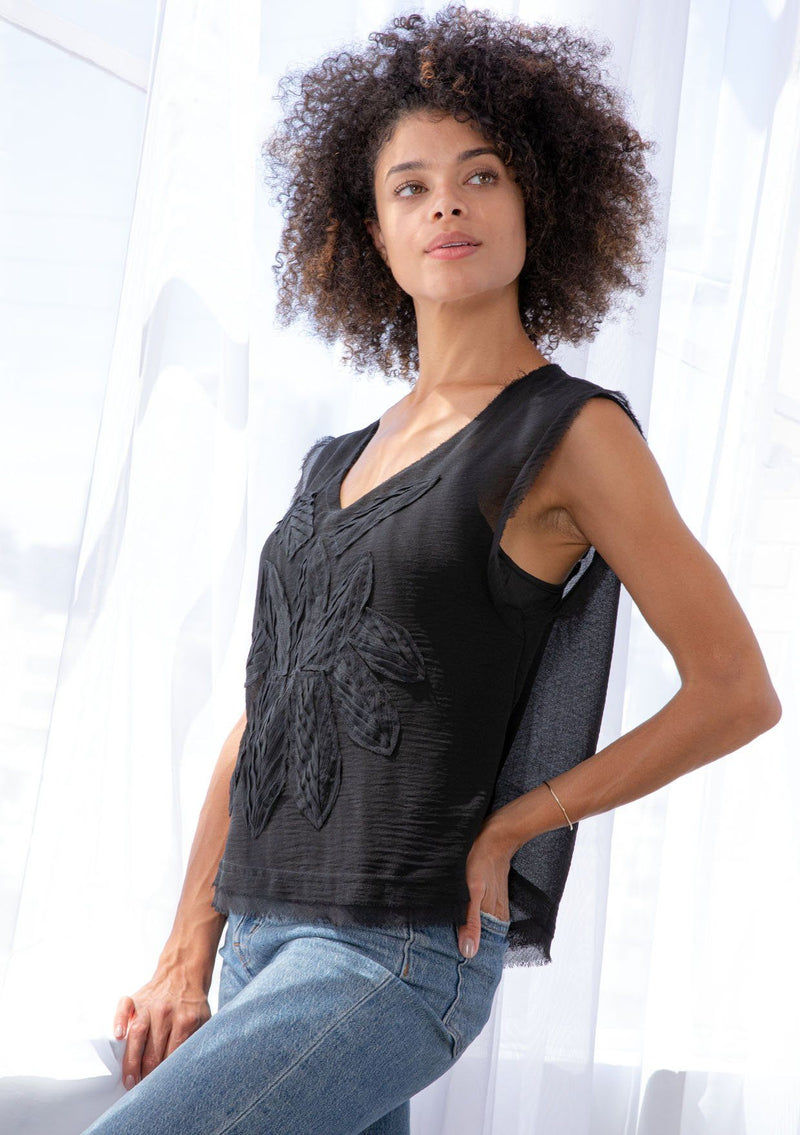 [Color: Black] A model wearing a sheer chiffon black top. With thick tank top straps, a raw hemline, and a pretty applique detail on the front. 