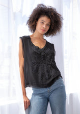 [Color: Black] A model wearing a sheer chiffon black top. With thick tank top straps, a raw hemline, and a pretty applique detail on the front. 