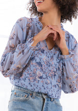 [Color: Light Blue] A model wearing a sheer peasant top in a vintage floral print. With a ruffled split neckline and long voluminous sleeves with a flounced wrist cuff.