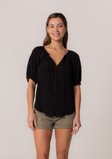 [Color: Black] A front facing image of a brunette model wearing a best selling button front blouse in black. With short puff sleeves, a button front, and a split v neckline with ties.