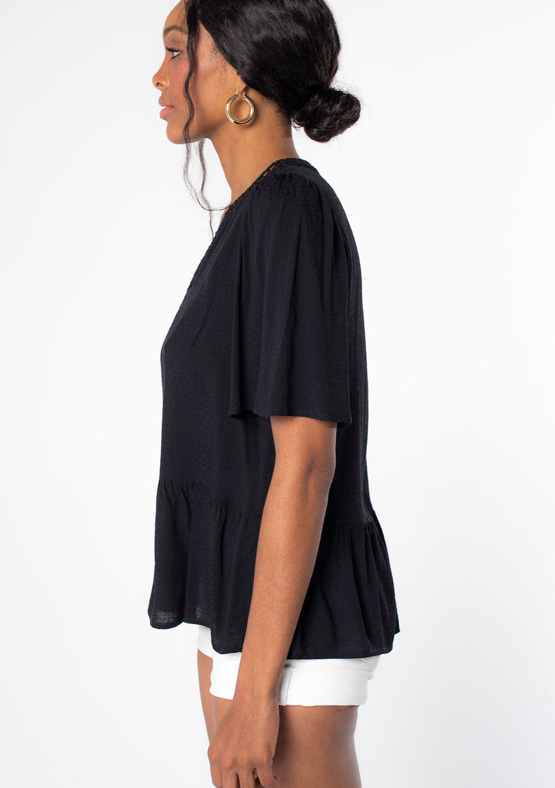 [Color: Black] A model wearing a flowy black short sleeve top.