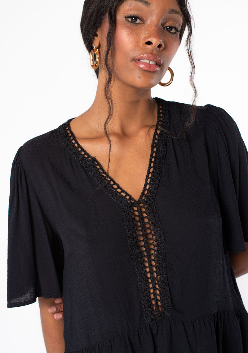 [Color: Black] A model wearing a flowy black short sleeve top.