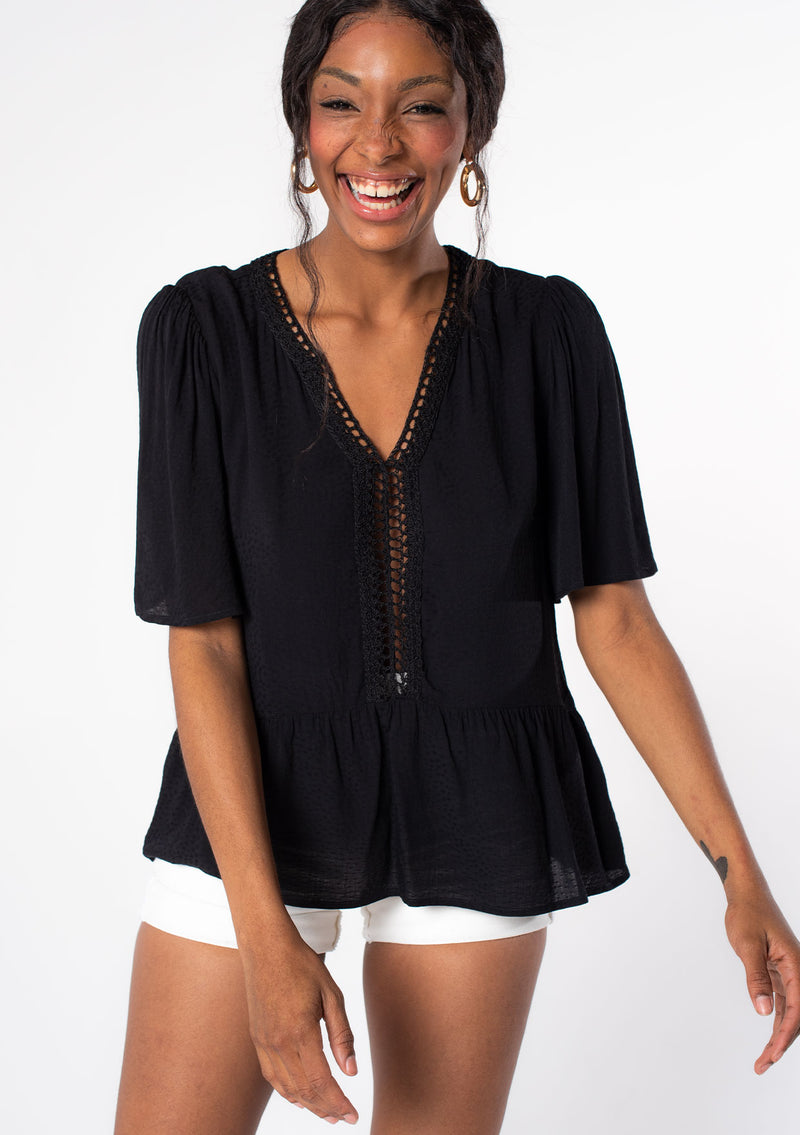 [Color: Black] A model wearing a flowy black short sleeve top.