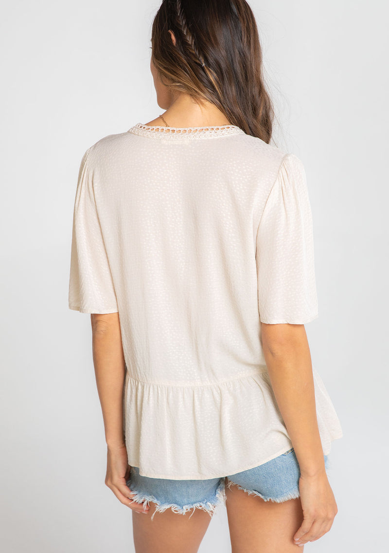 [Color: Vanilla Bean] A model wearing a flowy cream colored short sleeve top. 