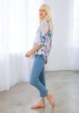 [Color: Ivory/Blue] A model wearing a sheer floral print bohemian blouse. With three quarter length raglan sleeves, an elastic cuff, a back keyhole detail with braided rope tie, and braided rope trim throughout. 