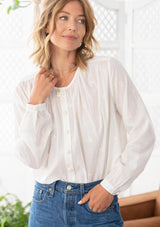 [Color: Cloud] A woman wearing a sheer cotton voile button front top. Featuring pretty floral embroidered details throughout, voluminous long sleeves with a button cuff closure, and a large button up front.