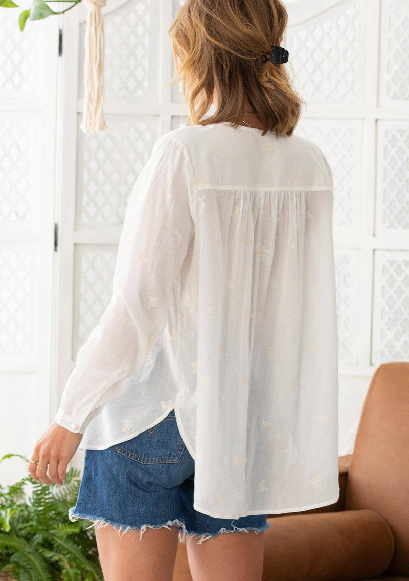 [Color: Cloud] A woman wearing a sheer cotton voile button front top. Featuring pretty floral embroidered details throughout, voluminous long sleeves with a button cuff closure, and a large button up front.