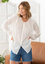[Color: Cloud] A woman wearing a sheer cotton voile button front top. Featuring pretty floral embroidered details throughout, voluminous long sleeves with a button cuff closure, and a large button up front.