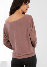 [Color: Nutmeg] A model wearing a nutmeg pink French terry top. With long dolman sleeves and a boat neckline that can be worn on or off the shoulder. 