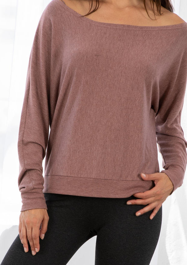 [Color: Nutmeg] A model wearing a nutmeg pink French terry top. With long dolman sleeves and a boat neckline that can be worn on or off the shoulder. 