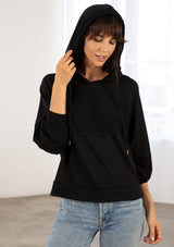 [Color: Black] A model wearing a black soft knit pullover sweatshirt. With a drawstring hoodie, long raglan sleeves, raw unfinished hemlines, exposed seams, and contrast inside out details. 