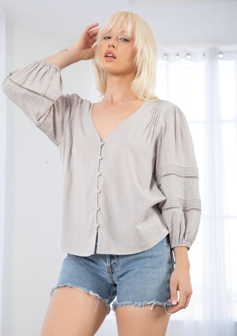 [Color: Silver] A model wearing a classic bohemian grey peasant top in a clip dot fabric. With three quarter voluminous sleeves, a self covered button front, a v neckline, and delicate pin tuck details throughout. 