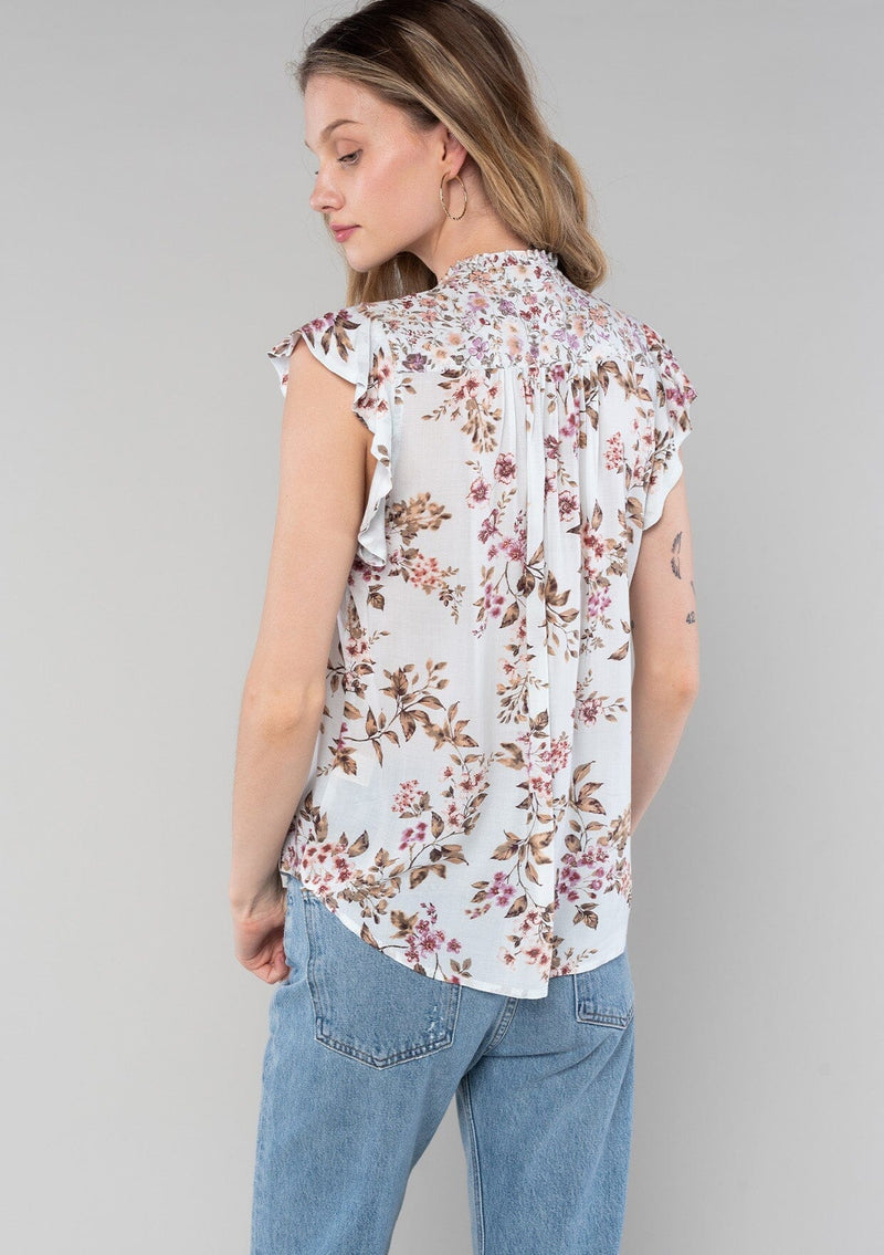 [Color: Mint/Rose] A back facing image of a blonde model wearing a spring bohemian top in a light mint and rose pink mixed floral print. With short flutter sleeves, a self covered button front, a ruffled neckline with ties, and a relaxed fit. 