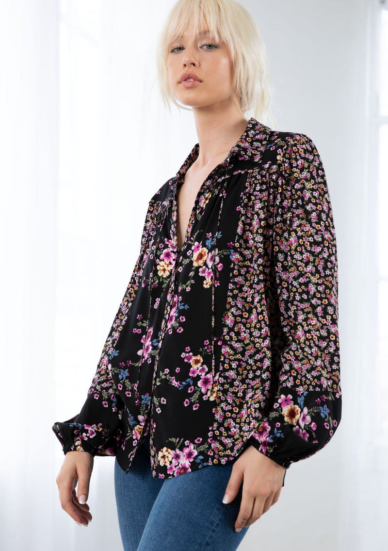 [Color: Black/Wine] A model wearing a classic bohemian button front blouse. With long voluminous sleeves, elastic wrist cuffs, a collared neckline with ties, and contrast ditsy floral print details. 