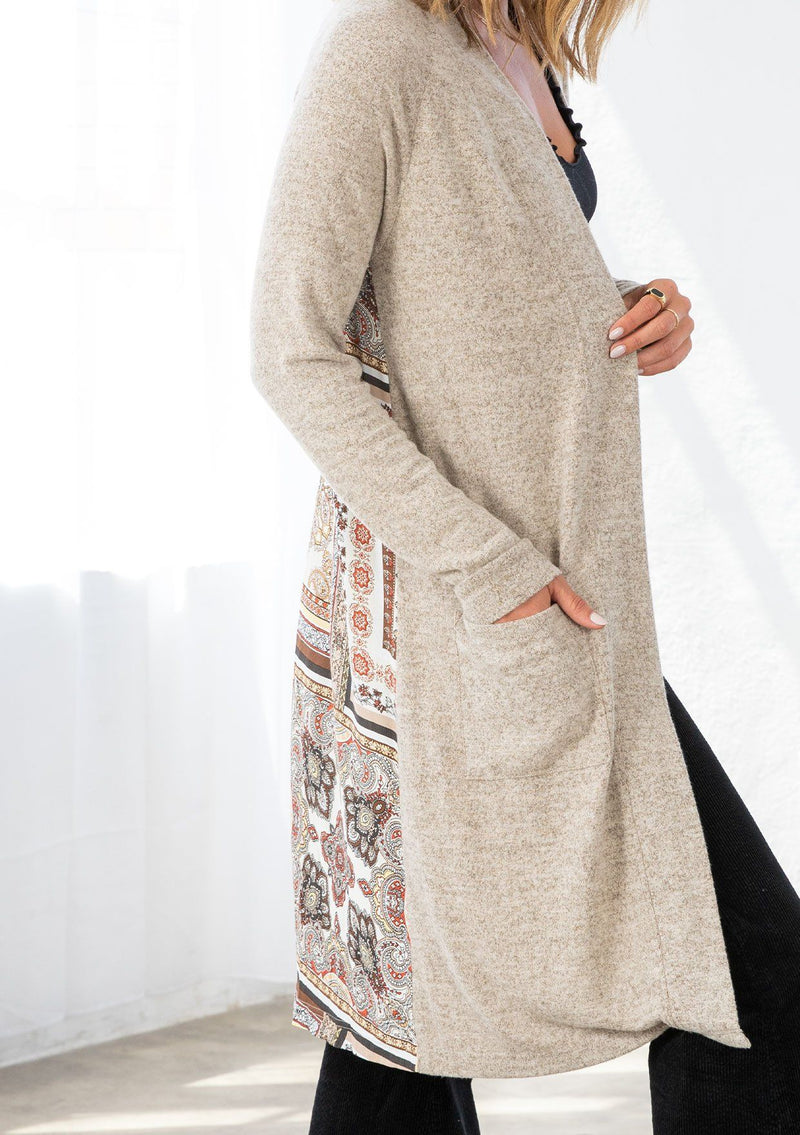 [Color: Ivory/Taupe] A model wearing a soft knit mid length cardigan with a contrast woven back in a patchwork print. With long sleeves, an open front, and two side patch pockets. 