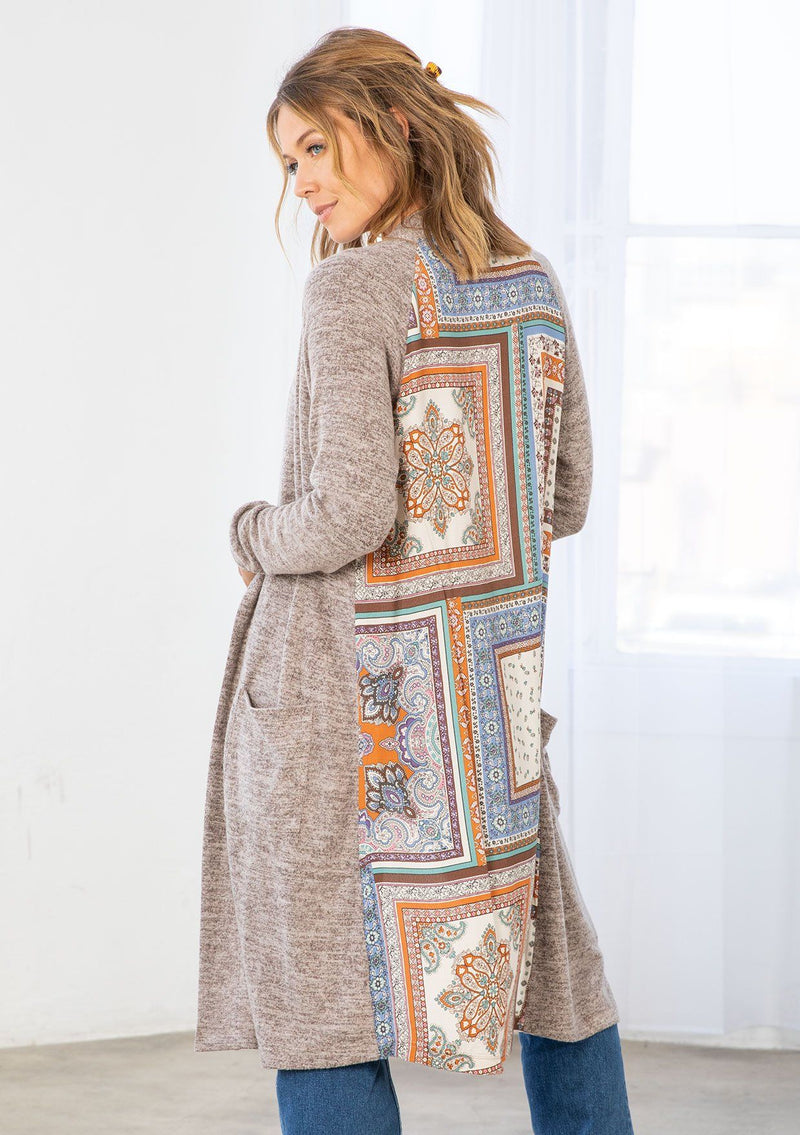 [Color: Natural/Periwinkle] A model wearing a soft knit mid length cardigan with a contrast woven back in a patchwork print. With long sleeves, an open front, and two side patch pockets. 