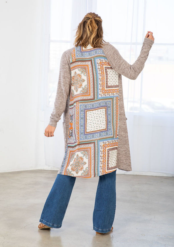 [Color: Natural/Periwinkle] A model wearing a soft knit mid length cardigan with a contrast woven back in a patchwork print. With long sleeves, an open front, and two side patch pockets. 