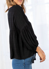 [Color: Black] A model wearing a slightly cropped classic black peasant top. Featuring a split v neckline with tassel ties, long voluminous balloon sleeves, and gathered details along the yoke. 