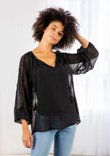 [Color: Black] A model wearing a sheer textured black peasant top with long voluminous sleeves, elastic wrist cuffs, a split v neckline with tassel ties, and delicate lace trim along the outer sleeve and center back. 