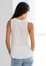 [Color: Ivory] A model wearing a sheer off white dot jacquard tank top with a crochet trimmed v neckline, a peplum waist, and thick tank top straps.