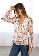 [Color: Pearl/Rose] A model wearing a pretty pink and ivory floral print bohemian blouse. A sheer top featuring a metallic clip dot detail throughout, a self covered loop button front, long sleeves with a double flounce cuff, and lace trim throughout. 