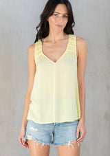 [Color: Yellow] A model wearing a flowy yellow bohemian tank top with a v neckline in front and back and braided trim details. 
