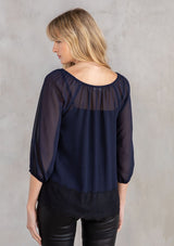 [Color: Navy/Black] A model wearing an ethereal sheer navy chiffon blouse with black eyelash lace trim hemline.