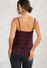 [Color: Black/Raspberry] A model wearing a black and raspberry pink ditsy floral print tank top in chiffon. With adjustable spaghetti straps, a scooped neckline, and gold thread trim detail. 