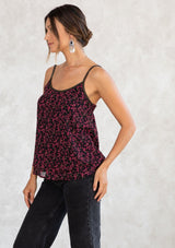 [Color: Black/Raspberry] A model wearing a black and raspberry pink ditsy floral print tank top in chiffon. With adjustable spaghetti straps, a scooped neckline, and gold thread trim detail. 