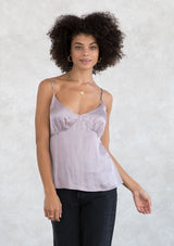 [Color: Lilac Mist] A model wearing an elevated lilac purple silky camisole with strappy back detail. With a v neckline, adjustable spaghetti straps, and a flattering relaxed silhouette. 