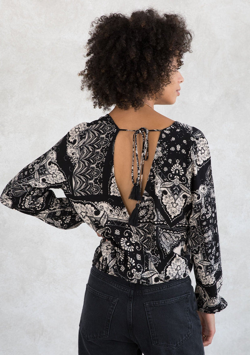 [Color: Black/Taupe] A model wearing a trendy black and taupe paisley bandana print surplice top. With voluminous long sleeves, a smocked elastic waist, and a v neckline. 