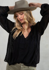 [Color: Black] Model wearing a black bohemian flowy top with swiss dot detail and long voluminous sleeves. 