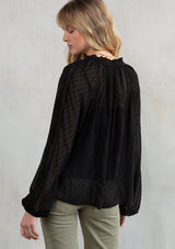 [Color: Black] Model wearing a black bohemian flowy top with swiss dot detail and long voluminous sleeves. 