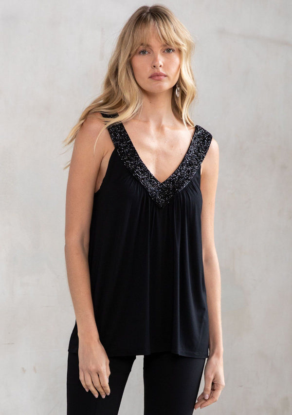 [Color: Black] A model wearing a black soft knit, holiday ready tank top with a beaded accent, a v neckline in front and back, and a flattering swing silhouette. 