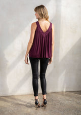 [Color: Fig] A model wearing a purple soft knit, holiday ready tank top with a beaded accent, a v neckline in front and back, and a flattering swing silhouette. 