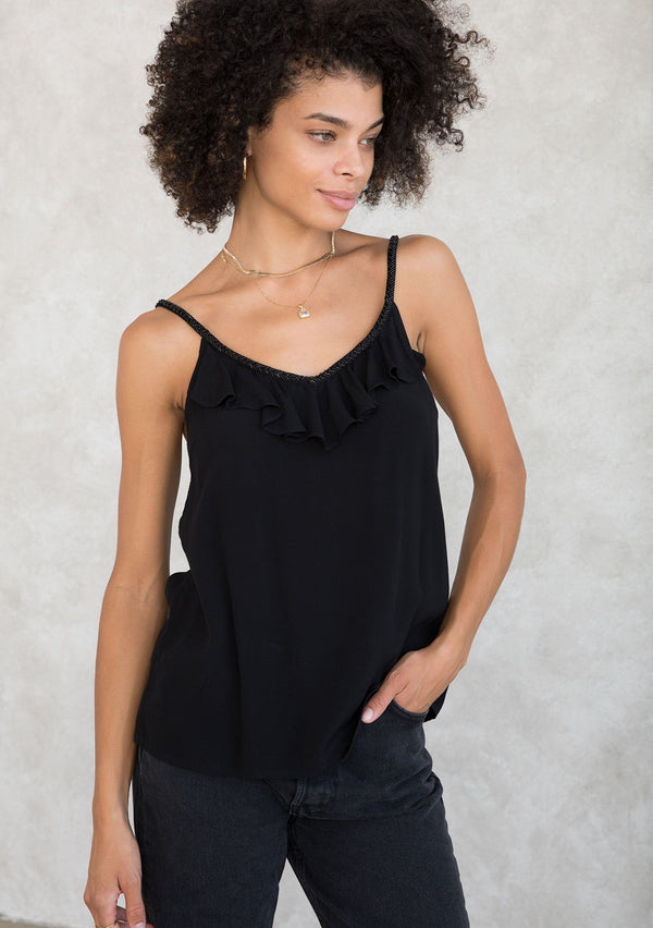 [Color: Black] A model wearing a Holiday ready black camisole. For your next special occasion, featuring a ruffle trimmed front and a beaded accent neckline with long beaded straps that tie in the back. 