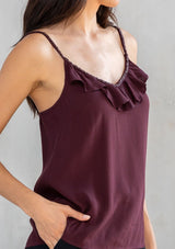 [Color: Fig] A model wearing a Holiday ready dark purple camisole. For your next special occasion, featuring a ruffle trimmed front and a beaded accent neckline with long beaded straps that tie in the back.